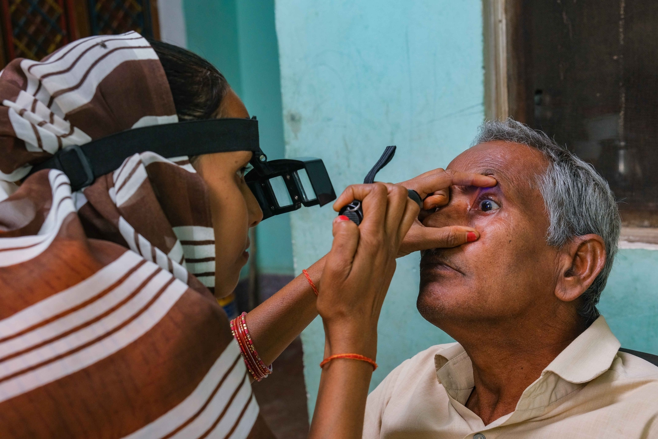 Community health worker performs an eye exam during a home visit.